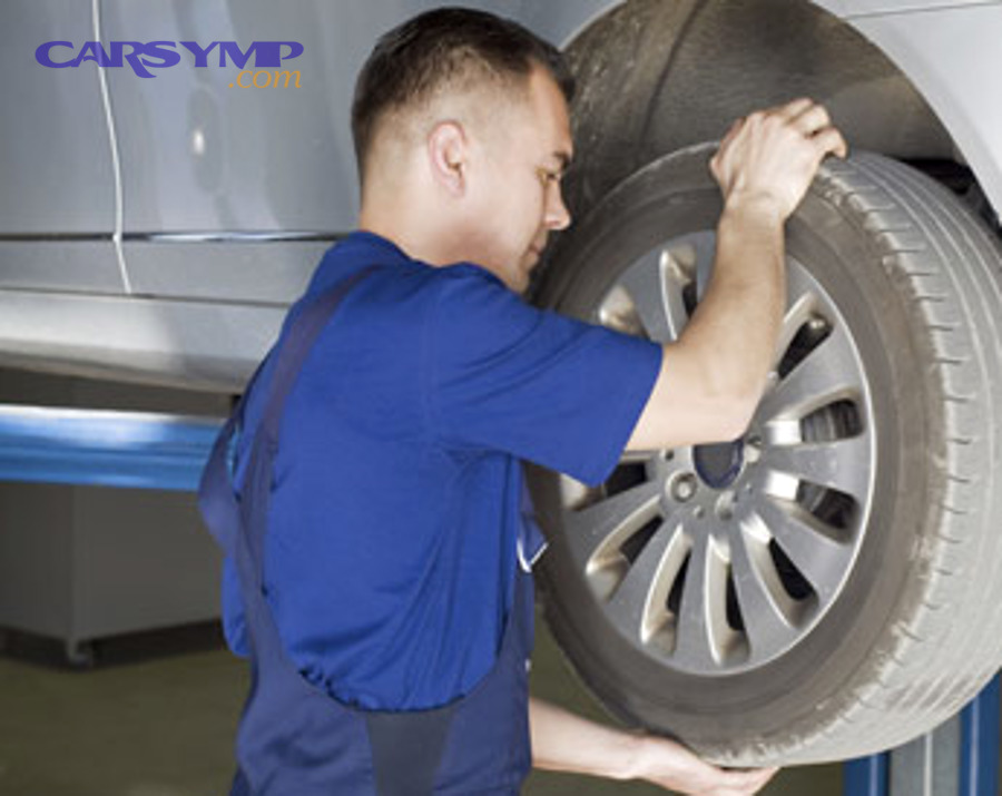 Technician inspecting front suspension and wheel on a lift