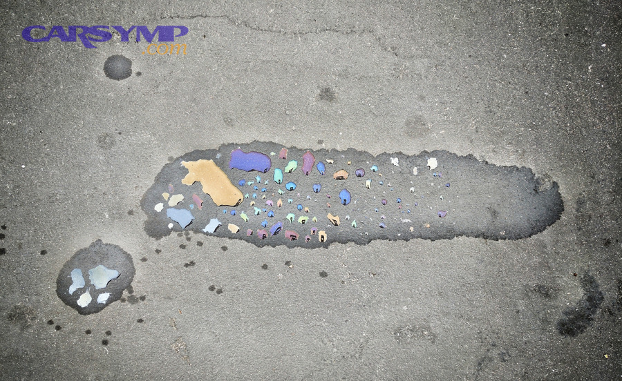Oil stain pattern on pavement resembling drips and spread from a leak