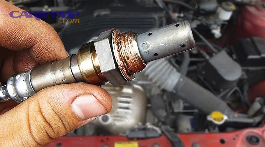 Technician holding oxygen sensor near exhaust under vehicle during replacement