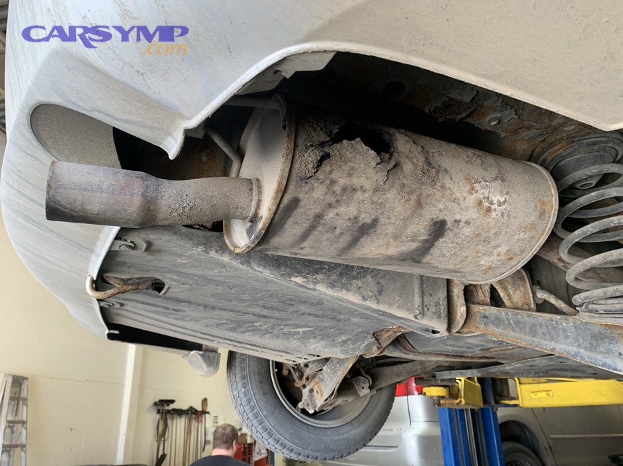 Technician checking a vehicle exhaust system for a leaking muffler at an inspection station
