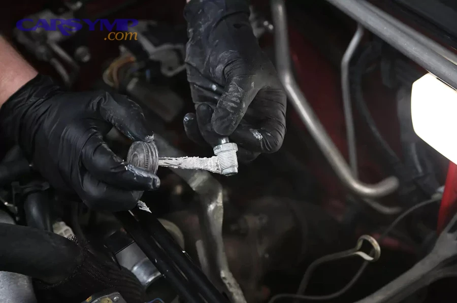 Mechanic applying sealant to a threaded PCV valve during replacement